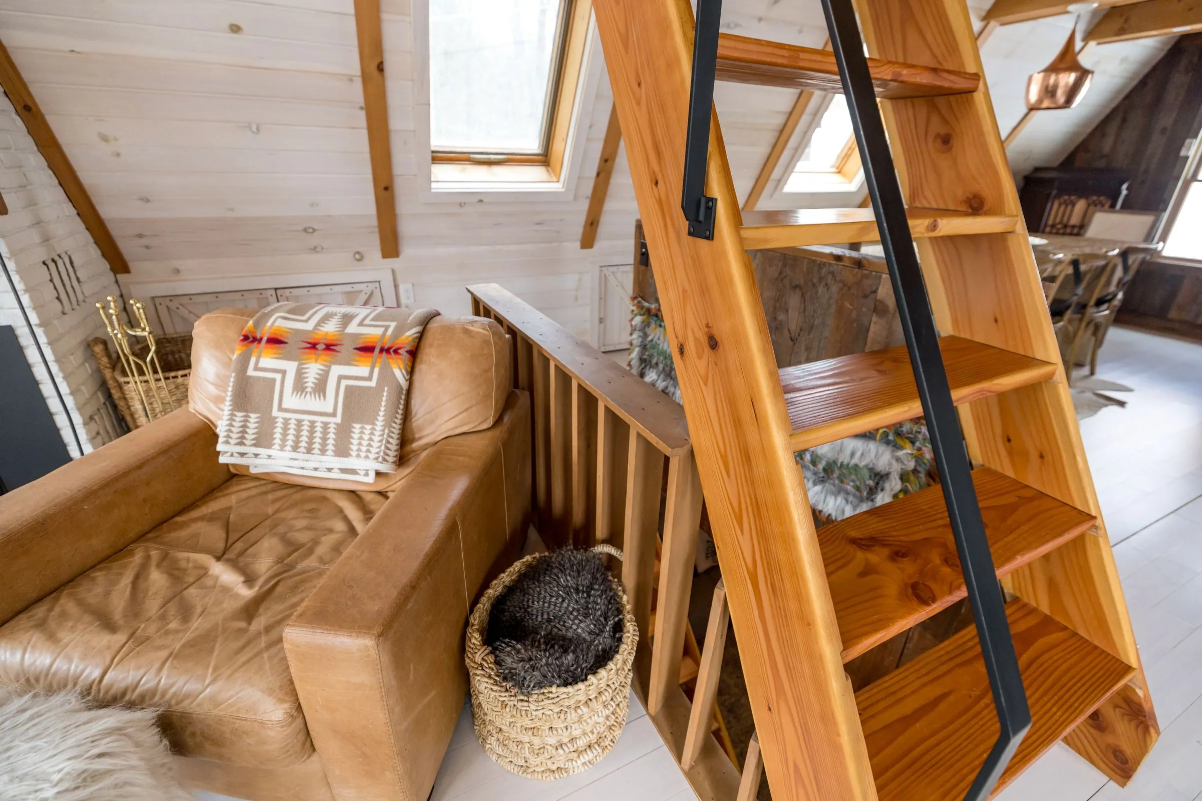 A wooden ladder up to a sleeping loft, beside a leather armchair