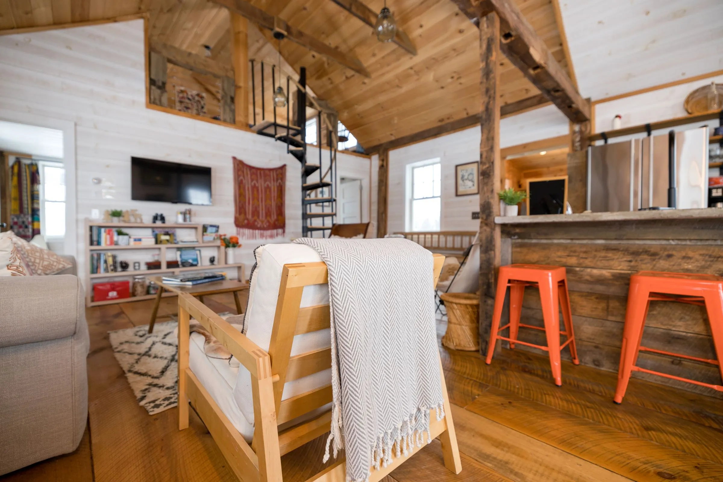 A bright cabin living room with a sofa, bookshelves and a kitchen counter