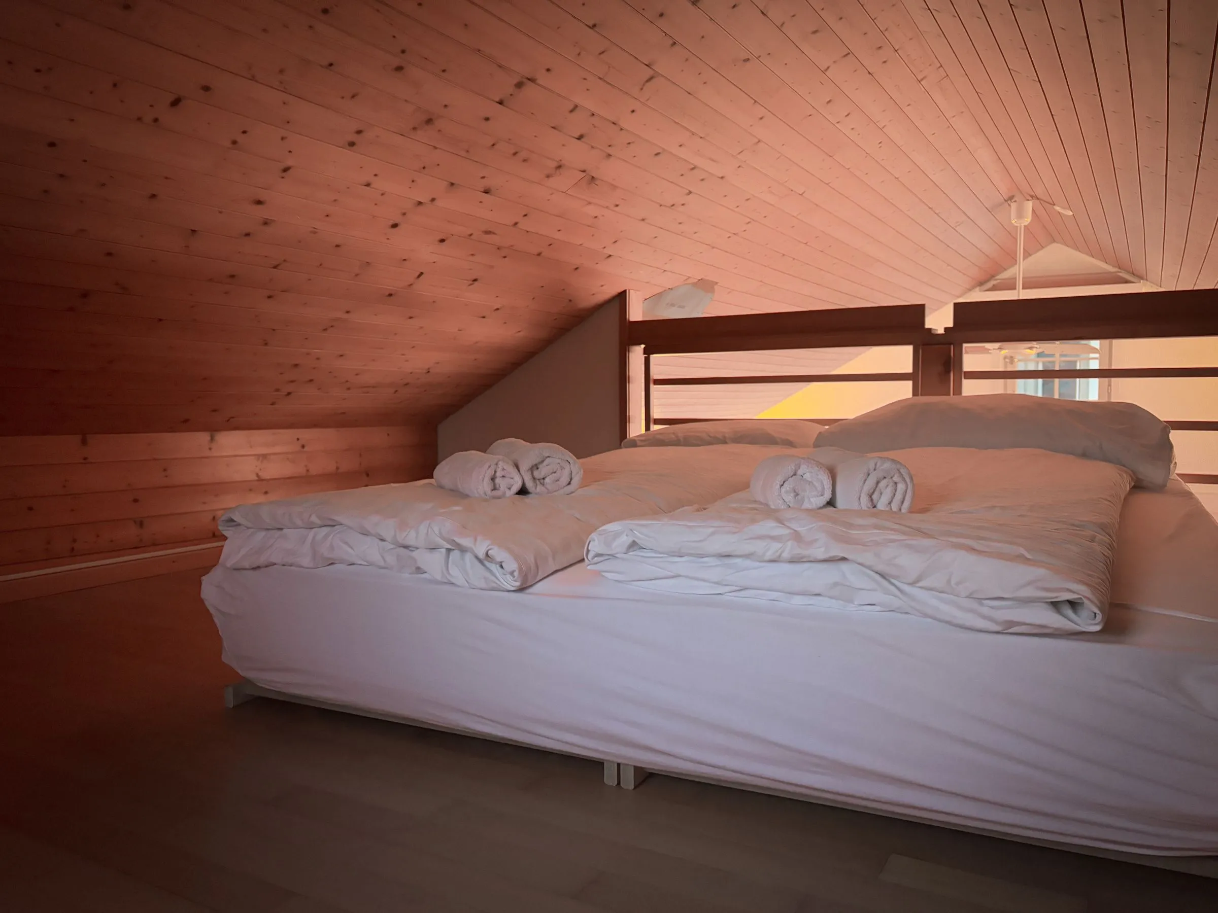 A loft bedroom under a timber ceiling, with fresh white bedding